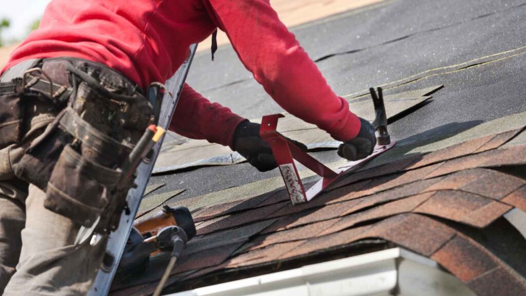 A person in a red jacket uses a tool to work on a roof