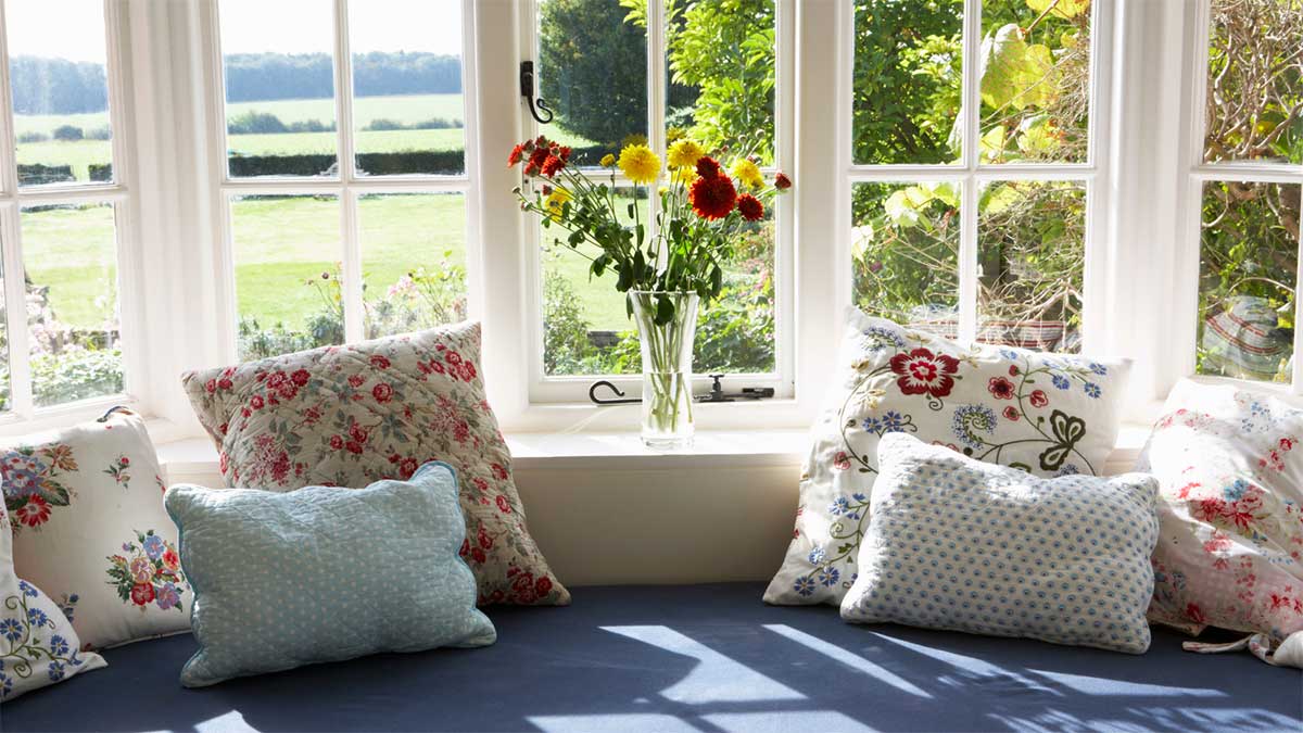 Cozy window seat with cushions overlooking a sunny garden.