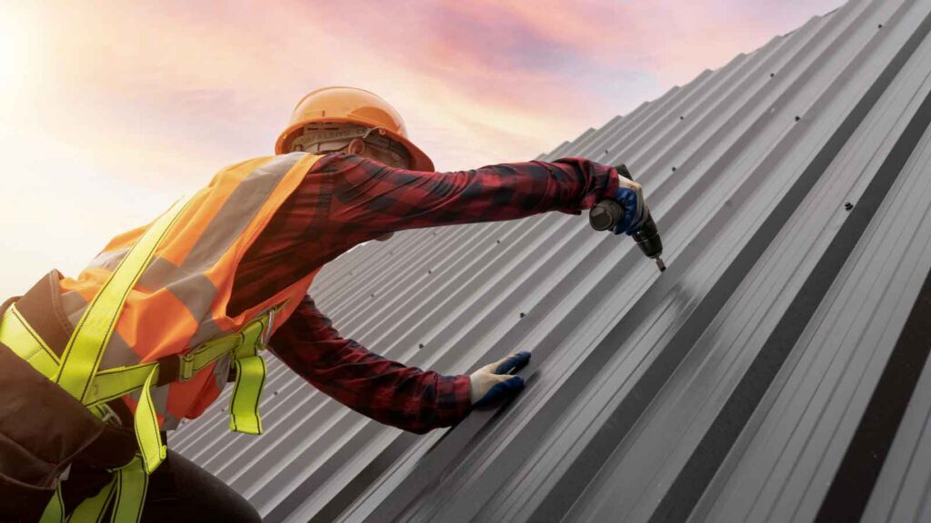 Worker securing metal roofing panels at sunset.