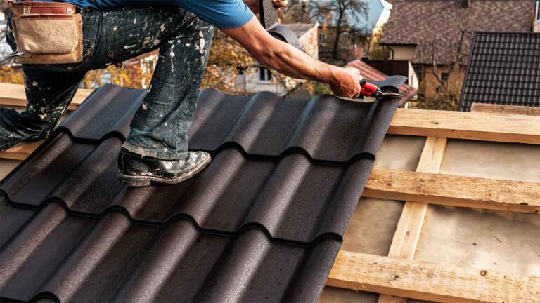 Roofer installing black metal tiles on a wooden roof frame