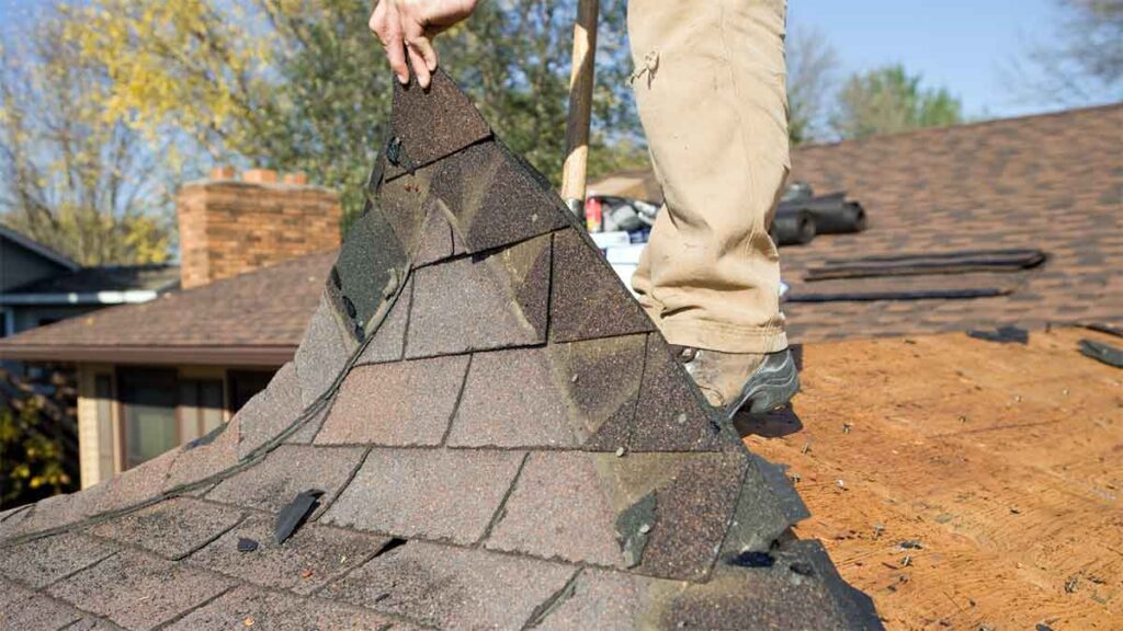 Worker removing old asphalt shingles during a roof replacement