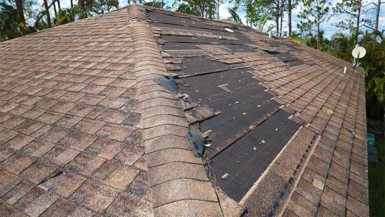 Damaged roof with missing and lifted shingles after a storm