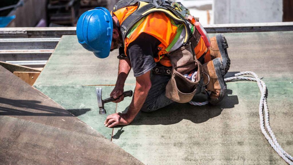 Construction worker hammering nails on a roof panel.
