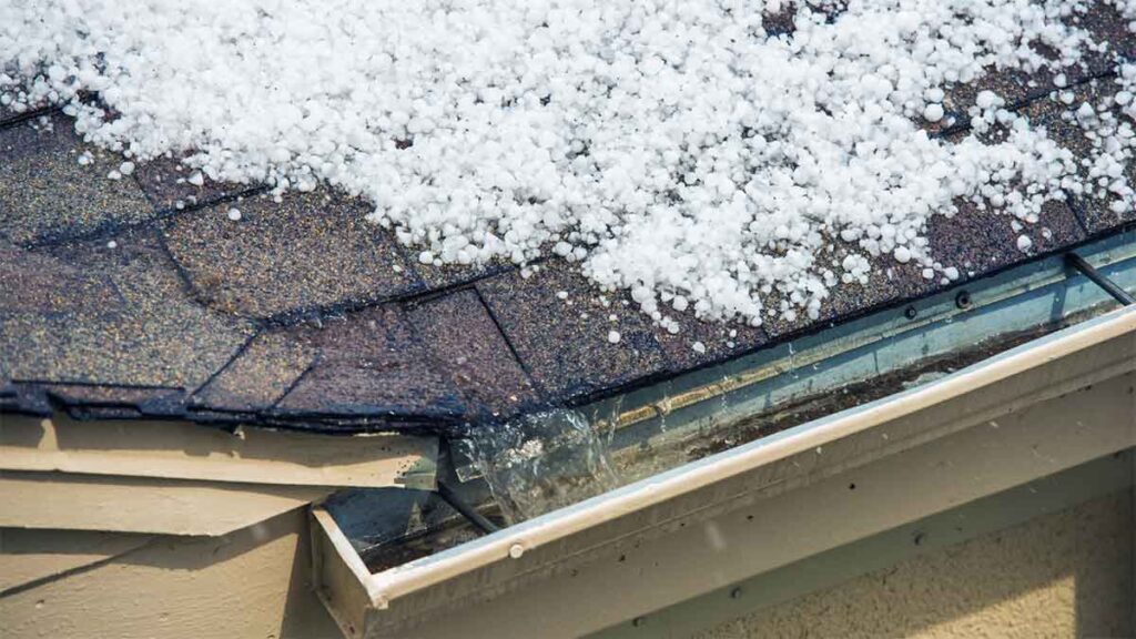 Hailstones covering an asphalt shingle roof and clogging the gutter.