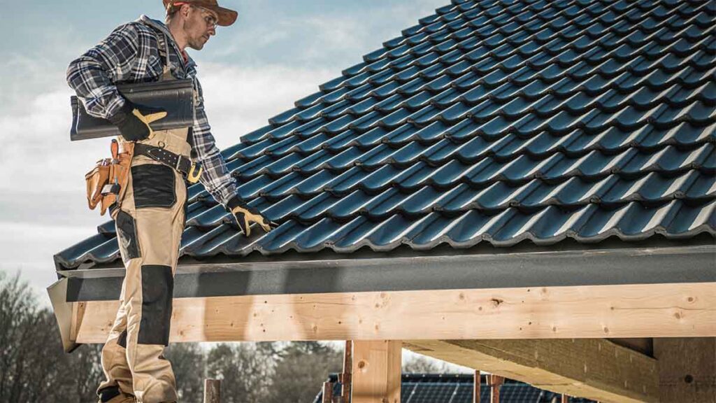 Roofer inspecting newly installed dark tile roofing on a wooden structure.