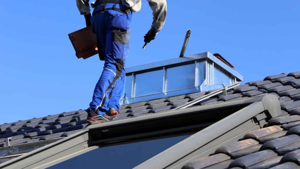 Roofer walks across a tiled roof holding repair materials.
