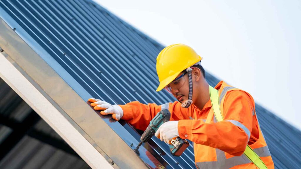 Worker drilling metal roofing panels on a building.