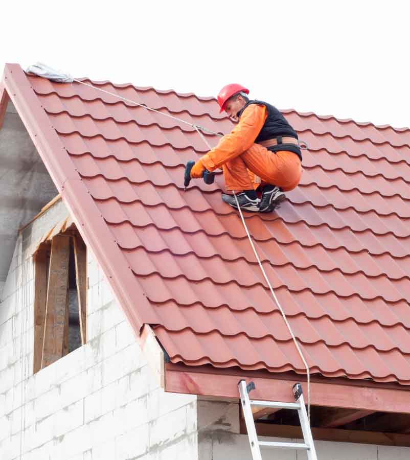 Worker securing red roof tiles on a pitched roof.