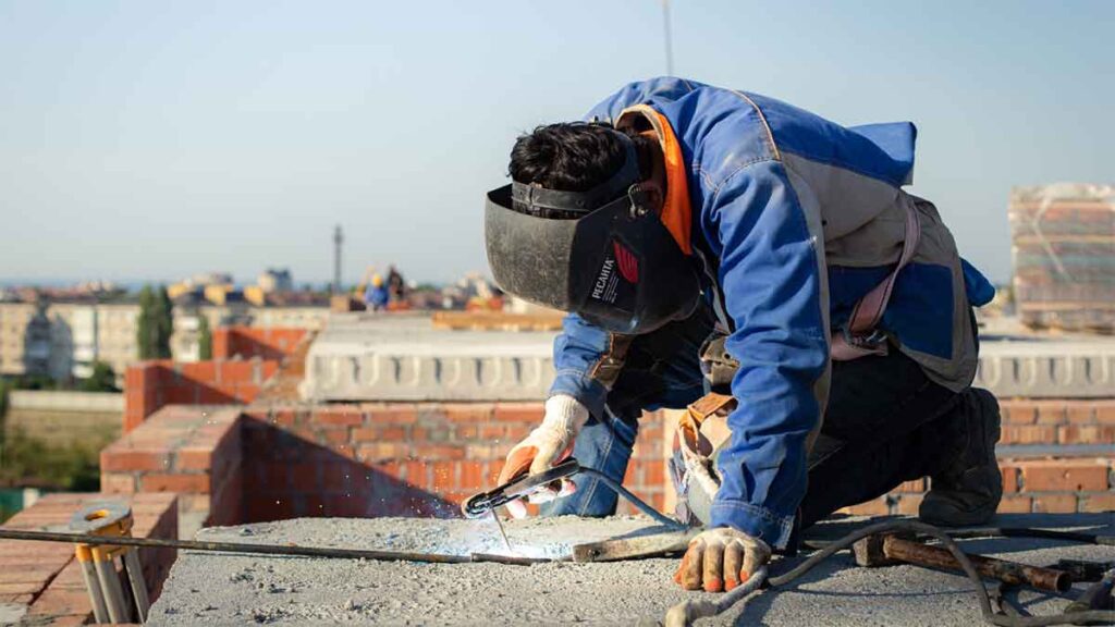Worker welding steel reinforcement on a rooftop construction site.