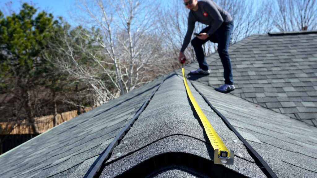 Worker measuring roof ridge with a tape measure.