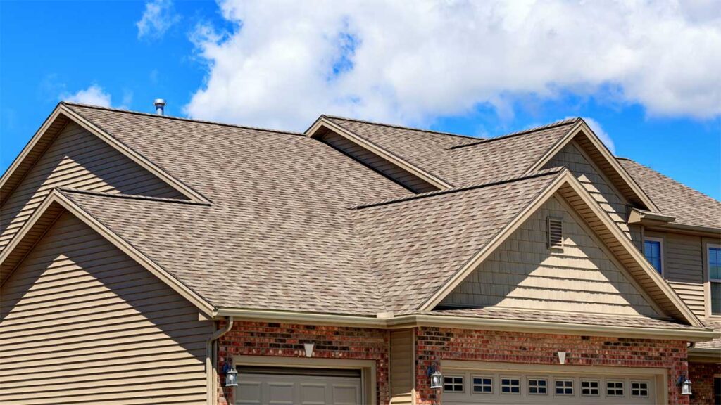 A house with a new asphalt shingle roof under a blue sky.