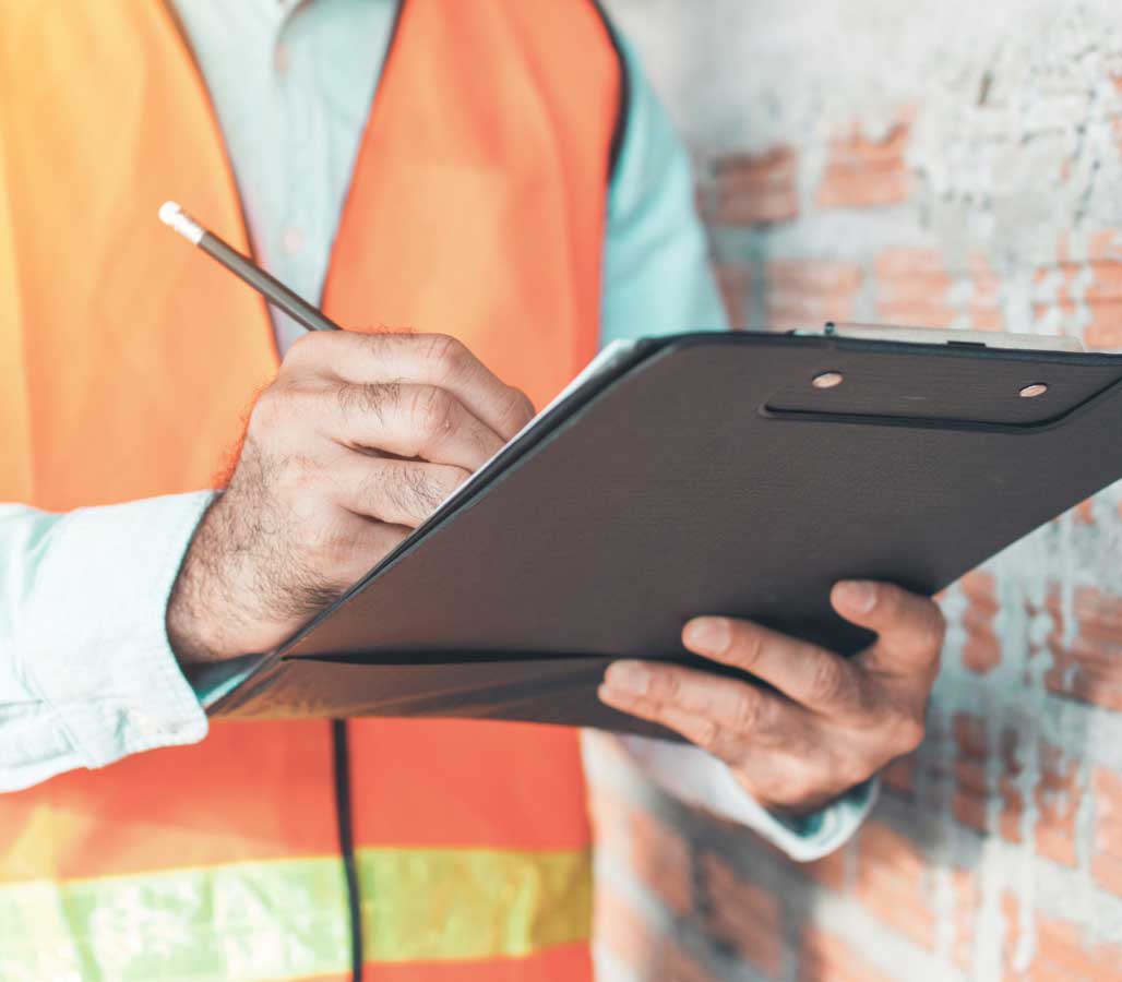 Inspector writing notes on a clipboard near a brick wall.