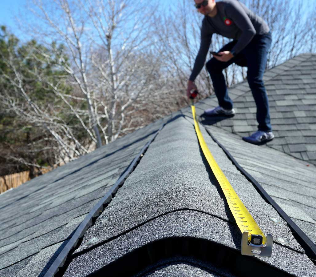 Person measuring roof ridge with a yellow tape measure.