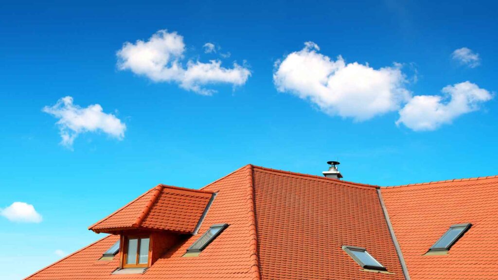  Red tile roof under a bright blue sky with scattered clouds.