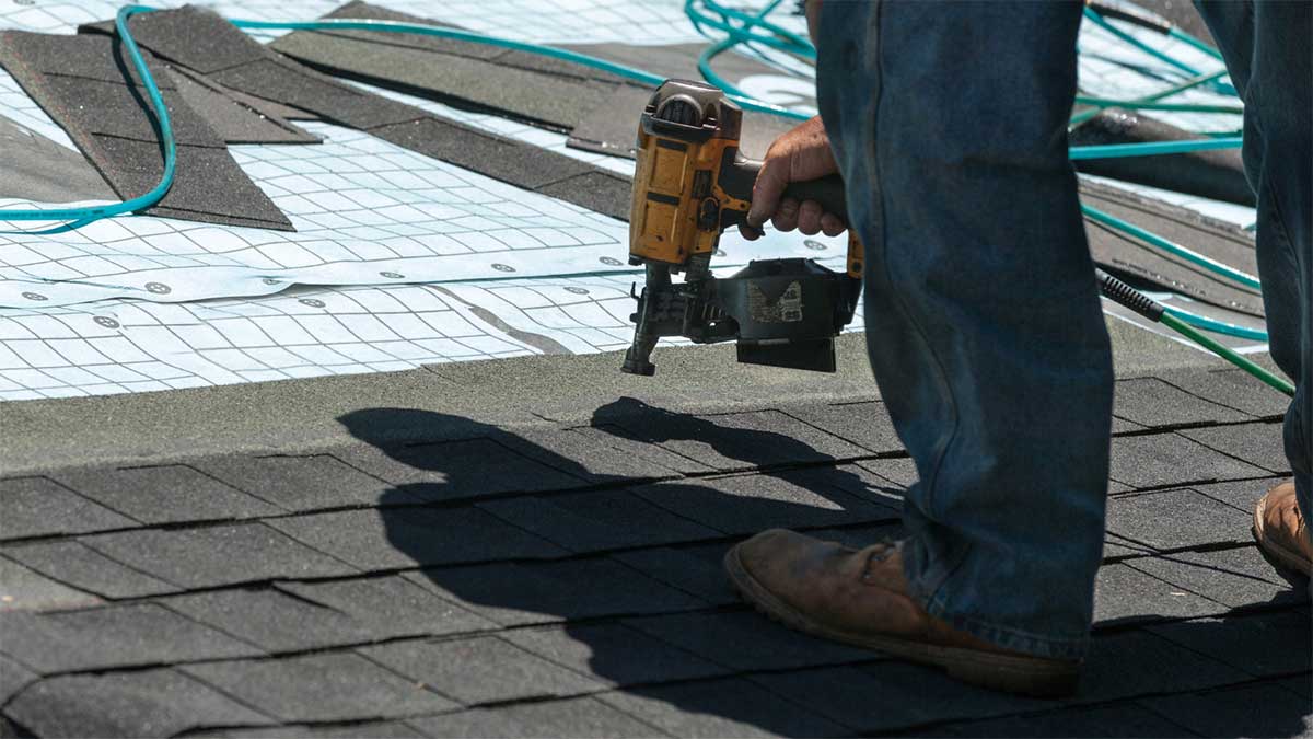 Worker removing old asphalt shingles during roof replacement.