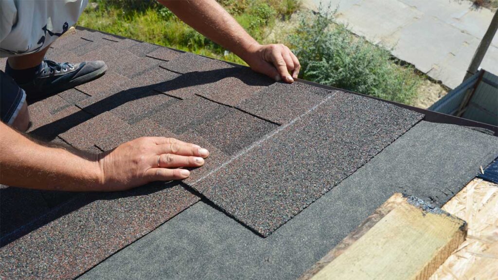 Worker installing asphalt shingles on a residential roof.
