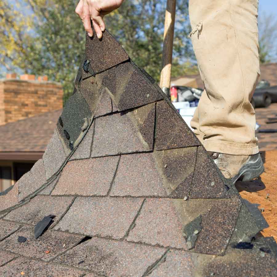 Worker removing old roof shingles during replacement.
