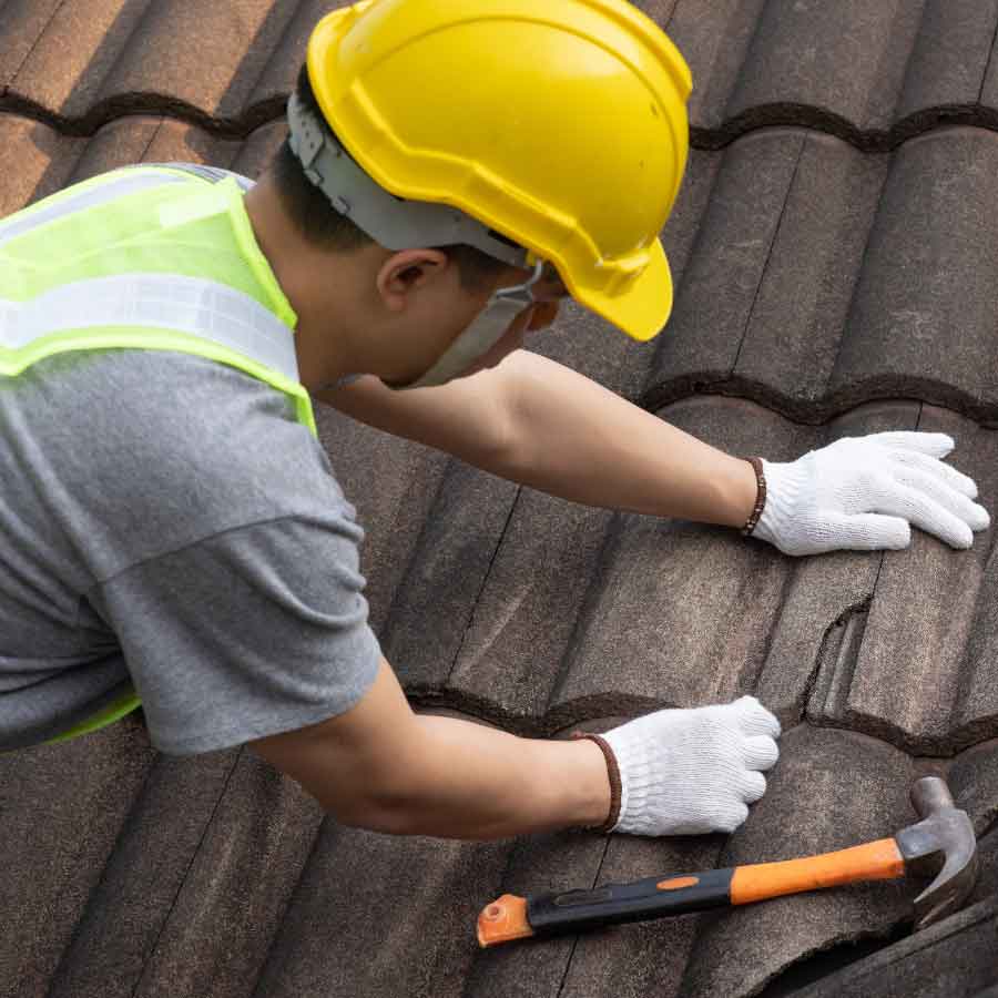 Worker repairing cracked roof tiles with a hammer nearby.