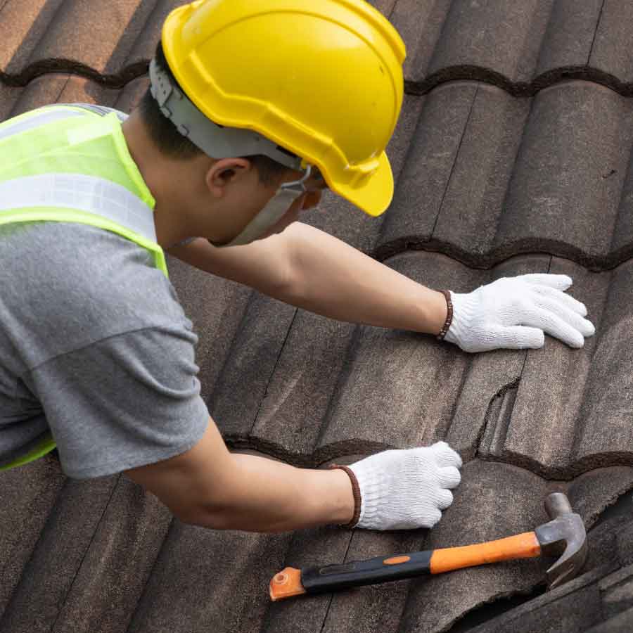 Worker repairing roof tiles with a hammer.