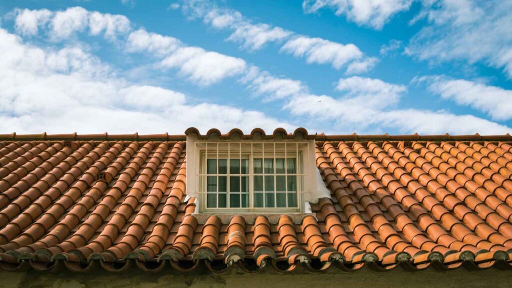 A red tile roof with a window under a clear blue sky.