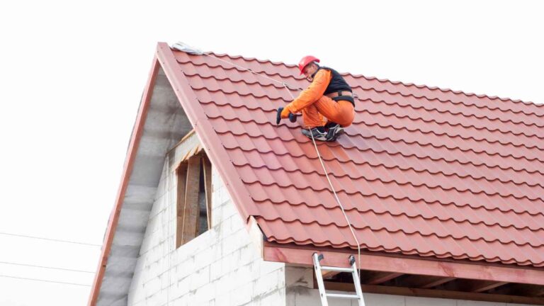 A worker installing red tile roofing on a house