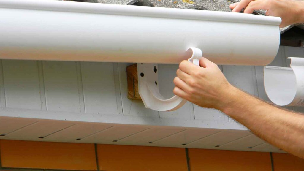 A worker drills screws into a metal roof panel