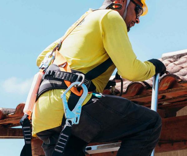 Roofer wearing safety gear inspects clay tile roofing.
