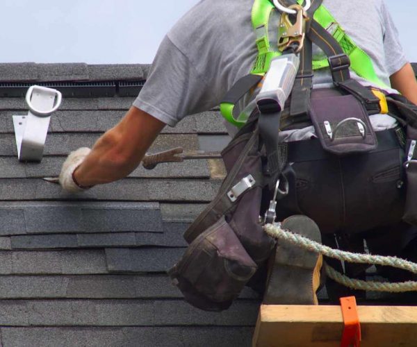 Roofersecuringshingleswhilewearingsafetygearonasteeproo