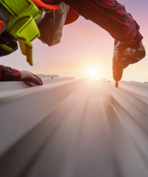 Worker drilling screws into metal roofing at sunrise.